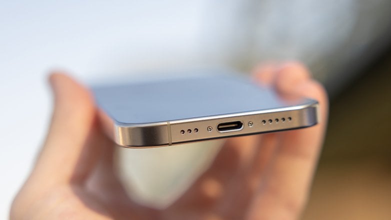 A hand holding the bottom edge of an iPhone 16 Pro, showing the USB-C port and speaker grilles.