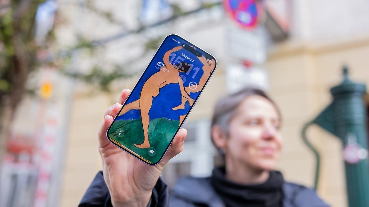 Una persona sosteniendo un iPhone 17 que muestra una obra de arte como fondo de pantalla con la hora 15:11.