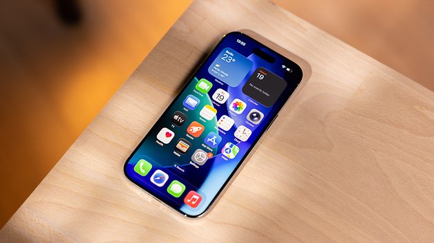 Ein iPhone mit einem bunten App-Layout auf einer Holzoberfläche, das Wetter- und Kalender-Widgets anzeigt.