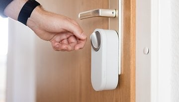 A hand reaching for a smart door lock installed on a wooden door.