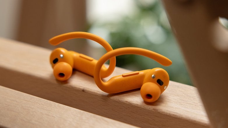 Des écouteurs sans fil Powerbeats Pro 2 orange reposent sur une surface en bois avec un flou de verdure en arrière-plan.