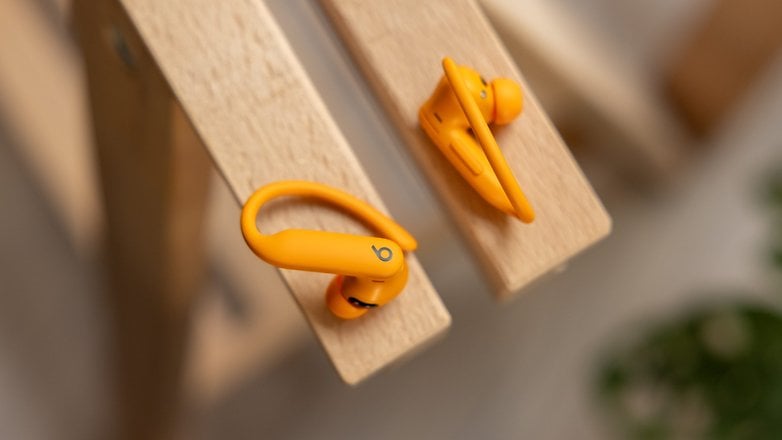 Wireless orange Beats Powerbeats Pro 2 earbuds resting on wooden surface.