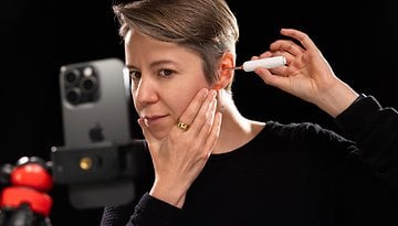 A person using a Bebird tool to clean their ear while a smartphone is set up to record the process.