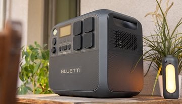 A Bluetti AC200L portable power station on a wooden table with a plant and a lantern nearby.