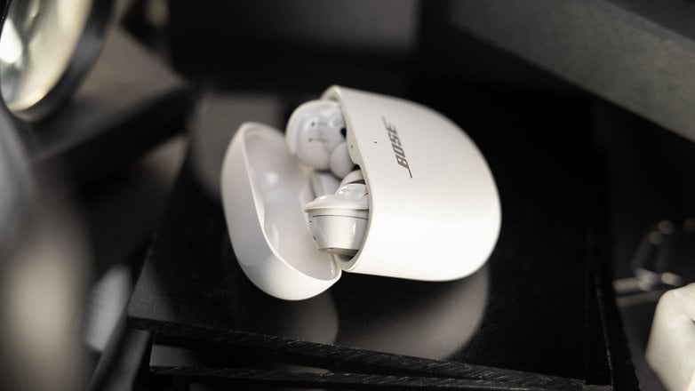 Les Bose QuietComfort Ultra Earbuds rangés dans leur boîtier posé sur une table avec son couvercle partiellement ouvert