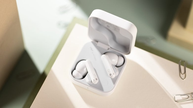 White wireless earbuds in their charging case on a light surface. White wireless earbuds in their charging case on a light surface.