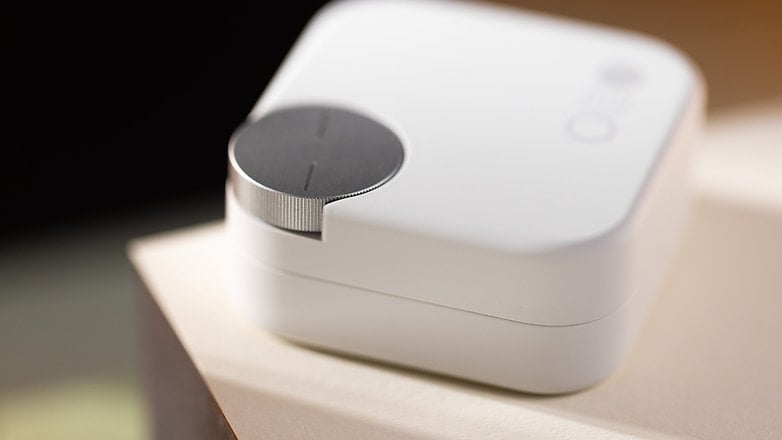 A compact white device with a circular control dial on top, resting on a light-colored surface. A compact white device with a circular control dial on top, resting on a light-colored surface.