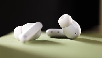 Wireless earbuds on a green surface, showcasing a sleek white design.