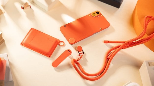 The CMF Phone 1 in its orange as seen from the back and placed flat on a table with its accesories.