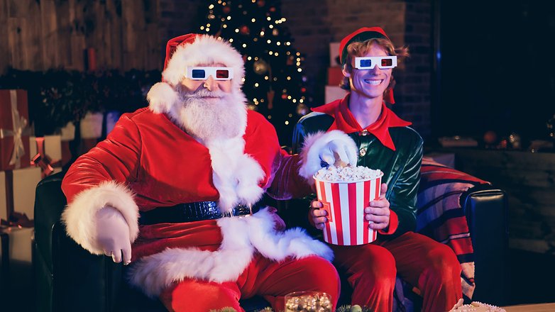 Ein Weihnachtsmann und ein Weihnachtself sitzen mit Popcorn auf dem Sofa