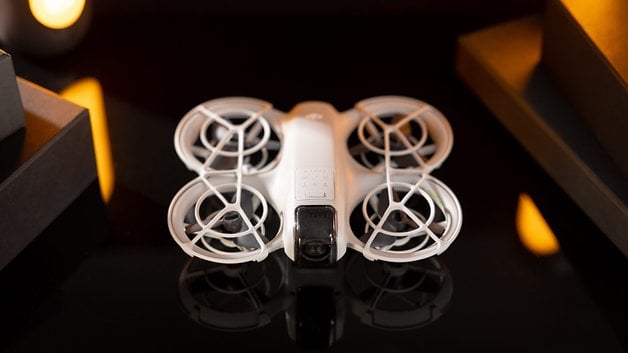 A white DJI Neo drone is shown on a reflective surface surrounded by its packaging.