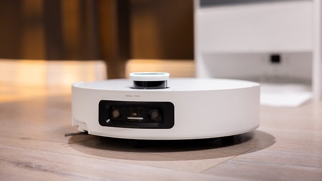 Ein weißer Roboterstaubsauger mit Sensoren auf einem Holzboden.