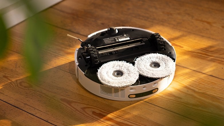 Robot vacuum cleaner with dual white mop pads, resting on wooden floor.