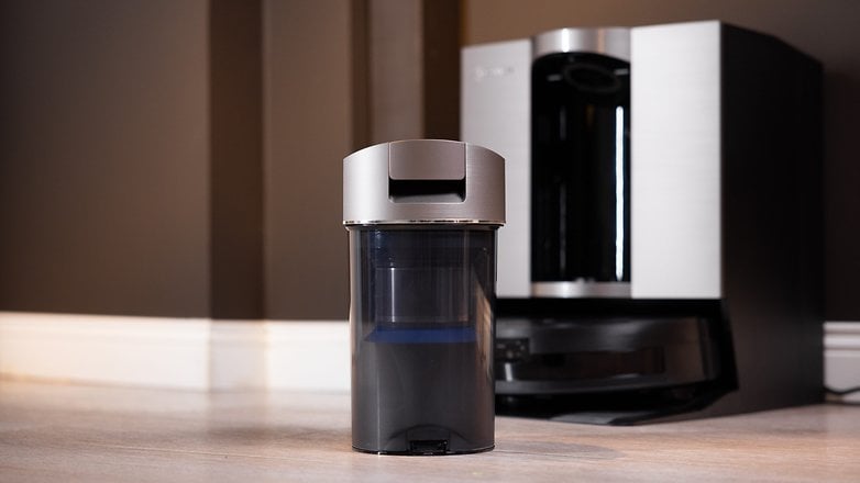 Eine Nahaufnahme des Ecovacs Deebot X11 OmniCyclone Staubbehälters auf einem Holzboden mit einem eleganten Gerät im Hintergrund. Eine Nahaufnahme des Ecovacs Deebot X11 OmniCyclone Staubbehälters auf einem Holzboden mit einem eleganten Gerät im Hintergrund.