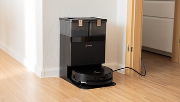 Un aspirateur robot Ecovacs Deebot X8 Pro Omni noir amarré à sa station de chargement dans une pièce.