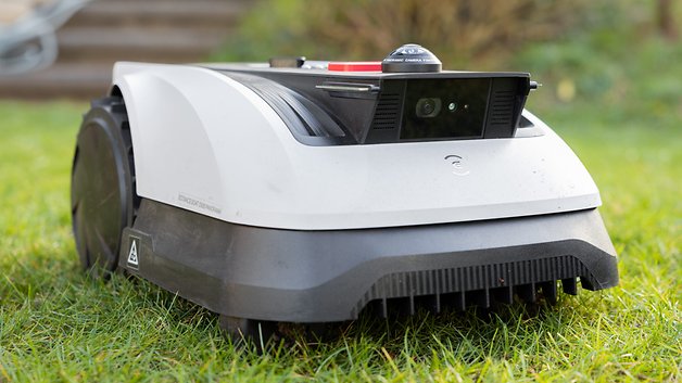 Une tondeuse robotisée est positionnée sur l'herbe, avec une caméra frontale et un design élégant.
