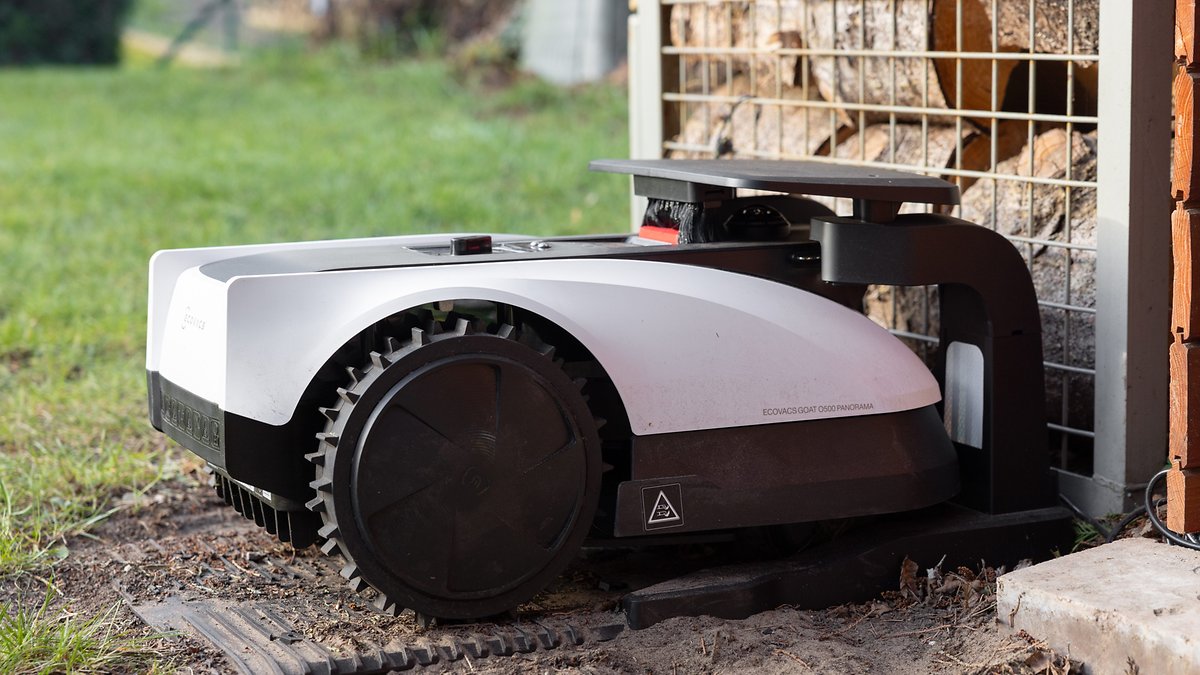 Une tondeuse robotique placée à côté d'une pile de bois.