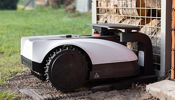 Une tondeuse robotique placée à côté d'une pile de bois.