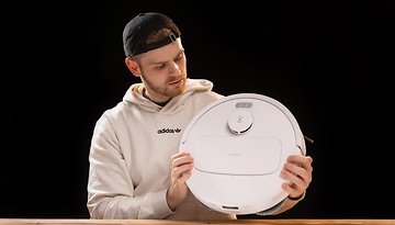 A man in a hoodie examines the ECOVACS N30 Pro Omni robotic vacuum cleaner.