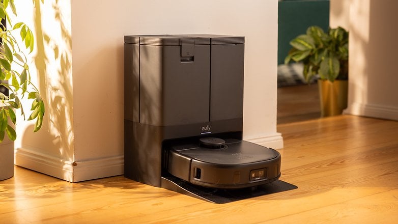 A Eufy X10 Pro Omni robotic vacuum docked next to a plant in a sunlit room. A Eufy X10 Pro Omni robotic vacuum docked next to a plant in a sunlit room.