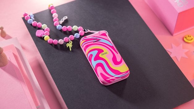 A colorful patterned phone in pink and yellow with a pearl strap on a black and pink background.