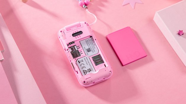 Un téléphone HMD Barbie rose montrant son compartiment à piles et un emplacement pour carte mémoire sur un fond rose.