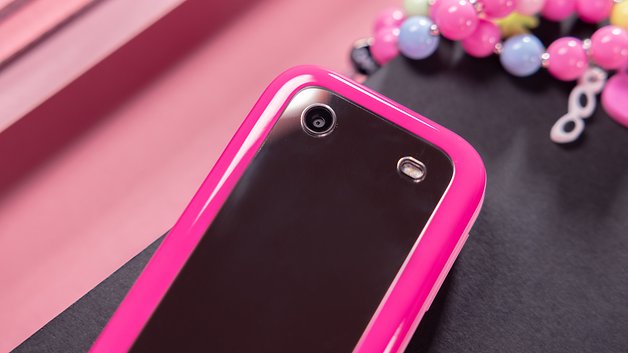 A close-up of a pink phone with a shiny back and two lenses, lying on a black surface.