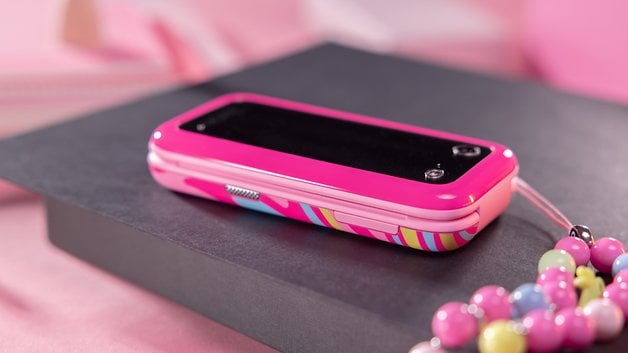 A pink Barbie phone with decorative pearls, resting on a black surface.