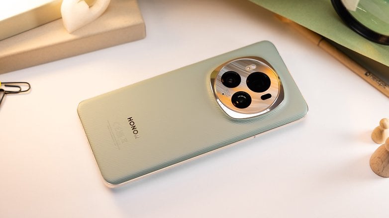 Ein auf der Rückseite liegendes Smartphone zeigt die strukturierte grüne Oberfläche und das kreisförmige Kameramodul mit einem dezenten Markenaufdruck an der Unterseite.