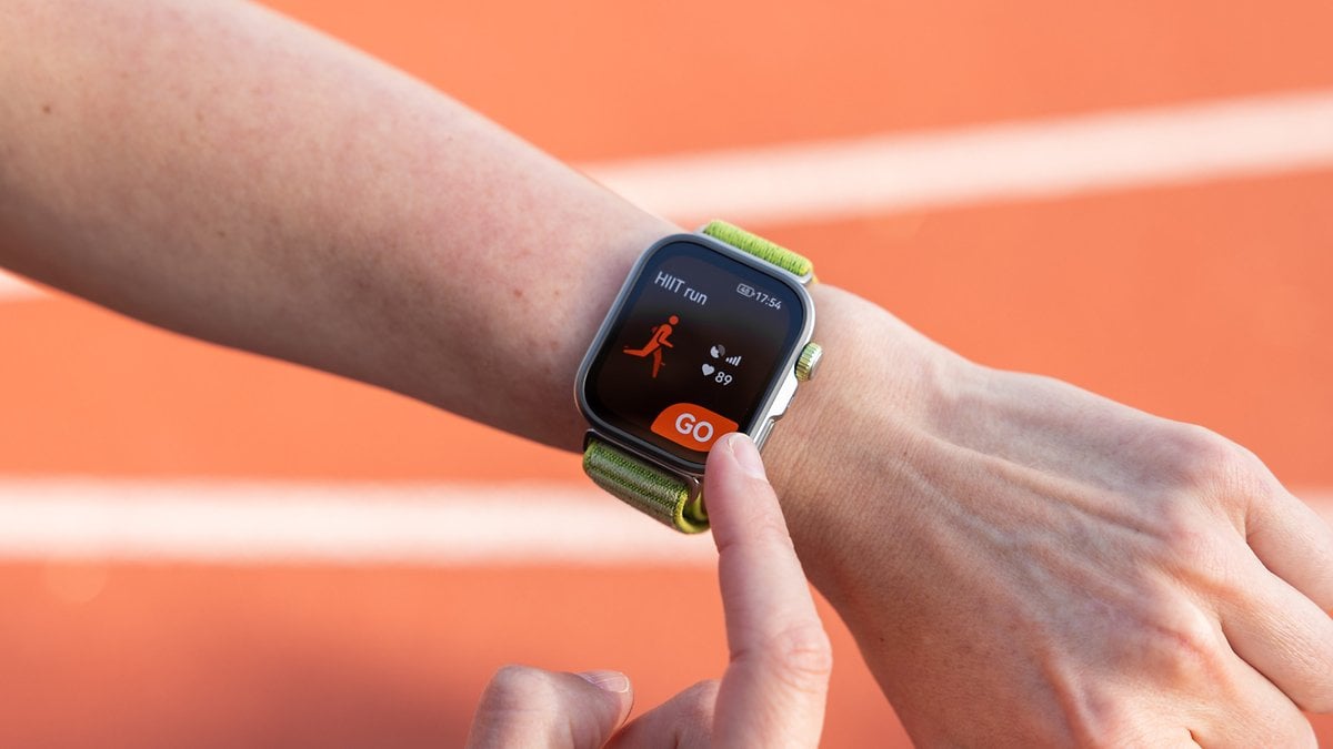 Une personne tient un smartphone affichant un plan d'entraînement 5K avec des indicateurs de performance sur une piste de course.