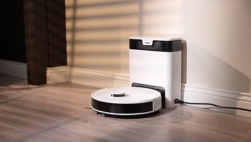 Ein Roboterstaubsauger neben einer Ladestation in einem gut beleuchteten Raum.