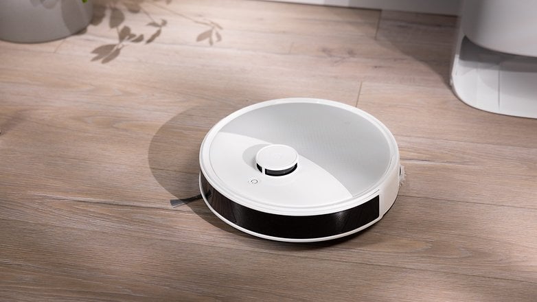 Ein weißer Roboterstaubsauger auf einem Holzboden. Ein weißer Roboterstaubsauger auf einem Holzboden.