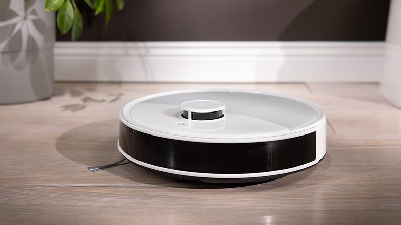 Ein Roboterstaubsauger auf einem Holzboden, mit einer Pflanze im Hintergrund. Ein Roboterstaubsauger auf einem Holzboden, mit einer Pflanze im Hintergrund.