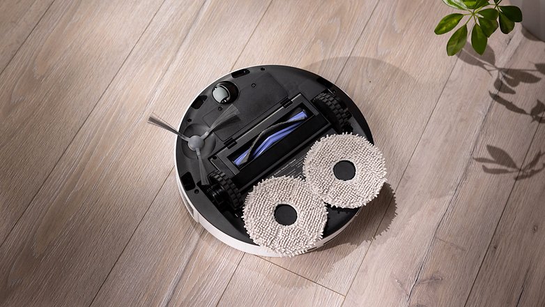 Ein runder, roboterhaftes Staubsauger mit zwei Reinigungspads auf einem Holzboden. Ein runder, roboterhaftes Staubsauger mit zwei Reinigungspads auf einem Holzboden.
