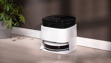 Ein moderner weißer und schwarzer Staubsauger auf einem Holzboden neben einer Pflanze.