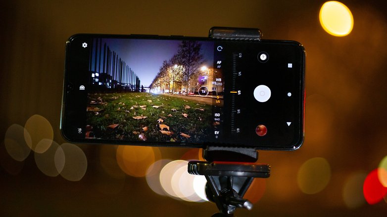 A smartphone mounted on a tripod, displaying a night photography scene with blurred lights in the background.