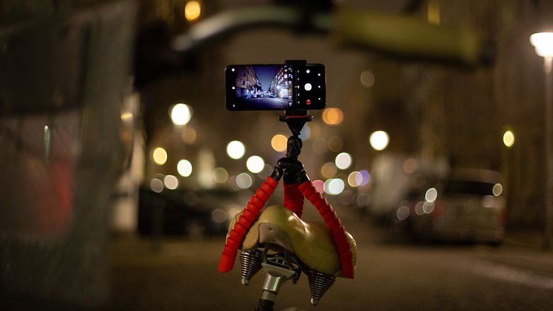 A smartphone mounted on a bicycle seat capturing a night scene with blurred city lights.