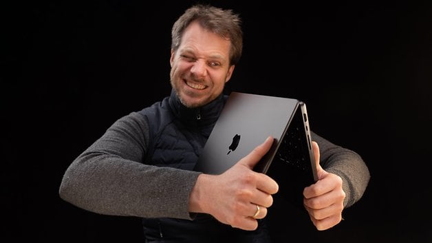 A man laughing while holding a MacBook Pro in front of a black background.