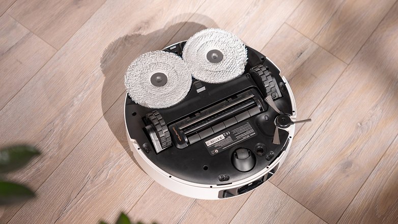 Obenansicht eines Mova P50 Pro Ultra-Roboterstaubsaugers mit zwei Reinigungspads auf einem Holzfußboden. Obenansicht eines Mova P50 Pro Ultra-Roboterstaubsaugers mit zwei Reinigungspads auf einem Holzfußboden.