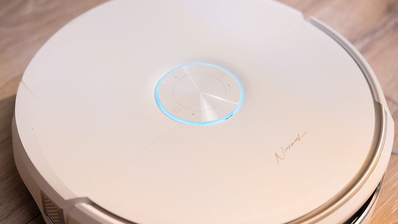 A sleek, round robotic vacuum cleaner with a blue light indicator on top. A sleek, round robotic vacuum cleaner with a blue light indicator on top.