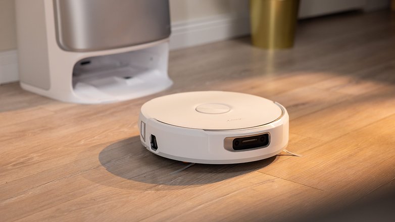 A white robotic vacuum cleaner on a wooden floor near a trash can. A white robotic vacuum cleaner on a wooden floor near a trash can.