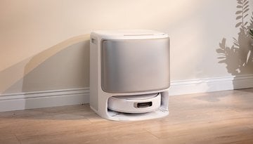 A modern, white automatic litter box on a wooden floor against a light-colored wall.