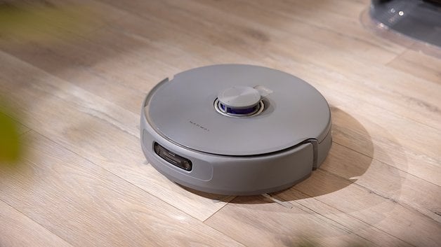 A grey robot vacuum cleaner on a wooden floor.