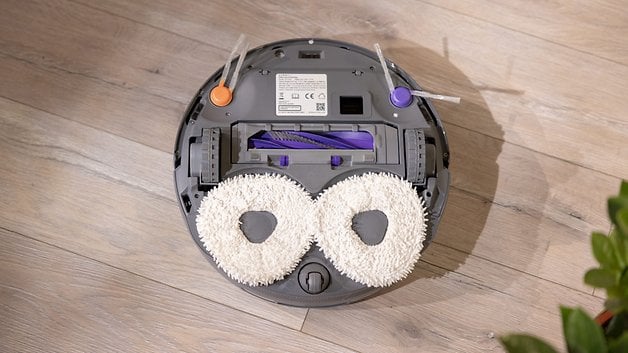 A robot vacuum cleaner with two round mop pads on a wooden floor.