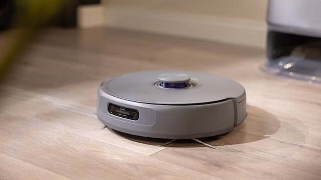 A grey robot vacuum cleaner on a wooden floor.