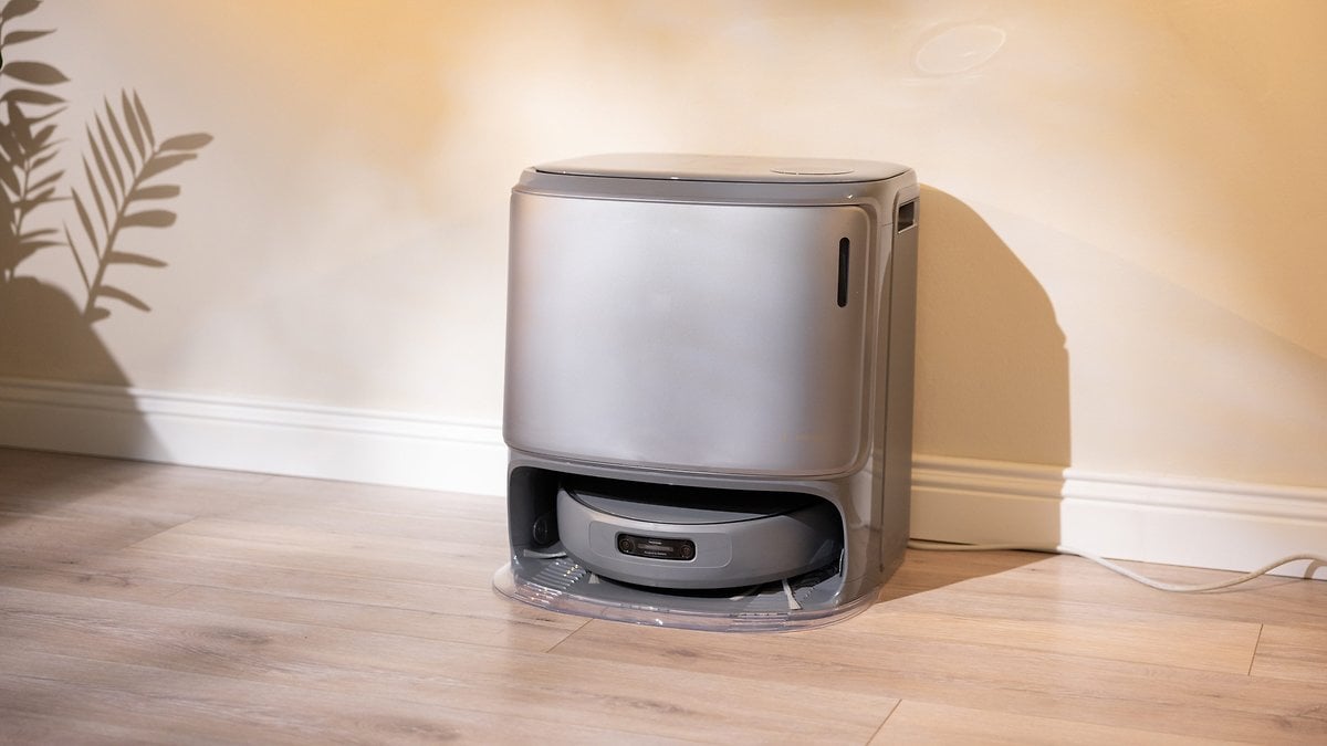 Un aspirateur robot gris élégant se trouve contre un mur dans une pièce bien éclairée.