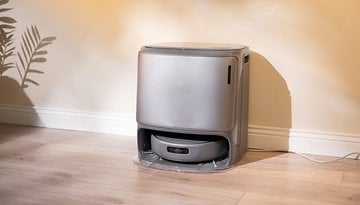 A sleek gray robotic vacuum cleaner sits against a wall in a well-lit room.
