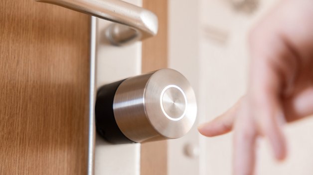 Nahaufnahme eines Nuki Smart Lock Pro an einer Tür mit einer Hand, die sich ihm nähert.