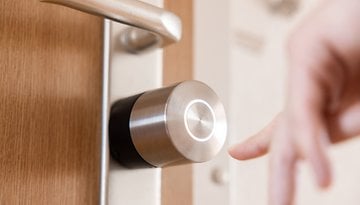 Nahaufnahme eines Nuki Smart Lock Pro an einer Tür mit einer Hand, die sich ihm nähert.