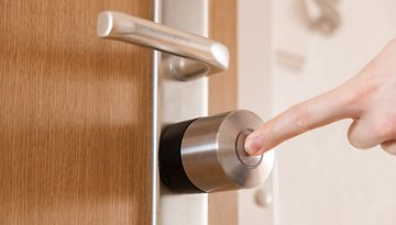 Eine Hand drückt den Knopf eines Nuki Smart Lock Pro, das an einer Holztür angebracht ist.